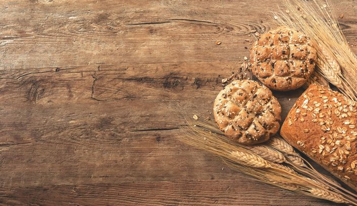 Broodjes en een brood met korenaren op een houten plank.