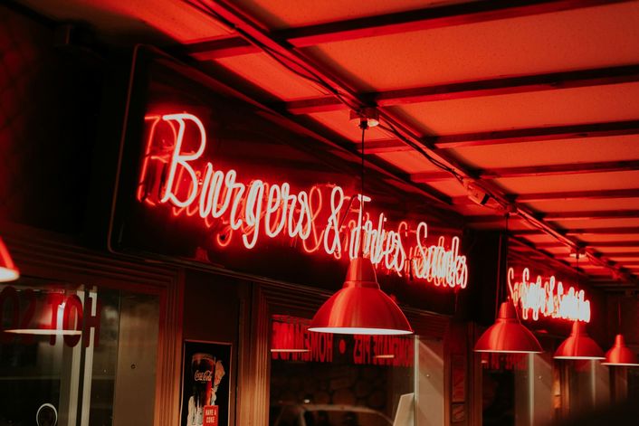 Een rood neonbord boven de bar van een burgerzaak, onder rode hanglampen.