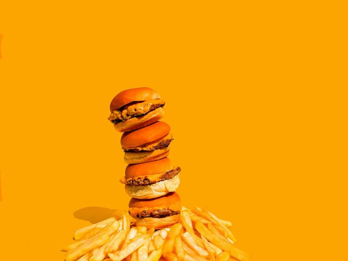 Four burgers stacked on a pile of fries against an orange background.