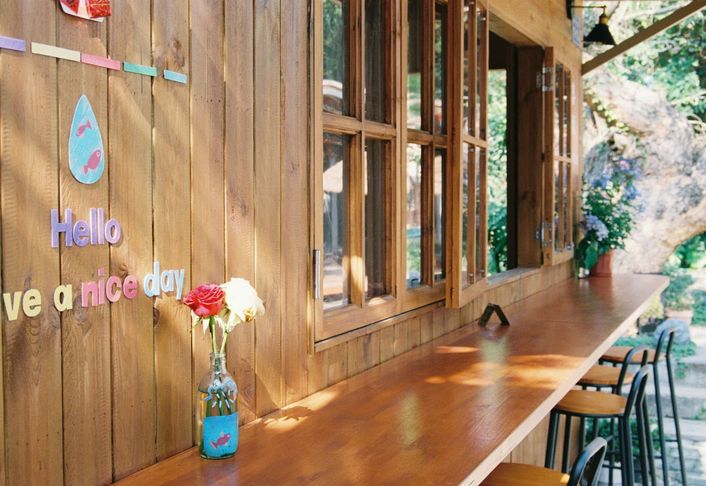 A wooden frontage with a long window counter, a small vase of roses and coloured letters on the wall.