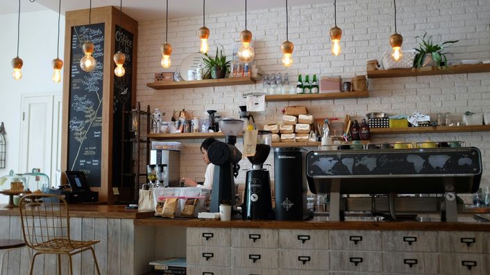 Een barista achter de toonbank bij een espressomachine, onder hanglampjes.