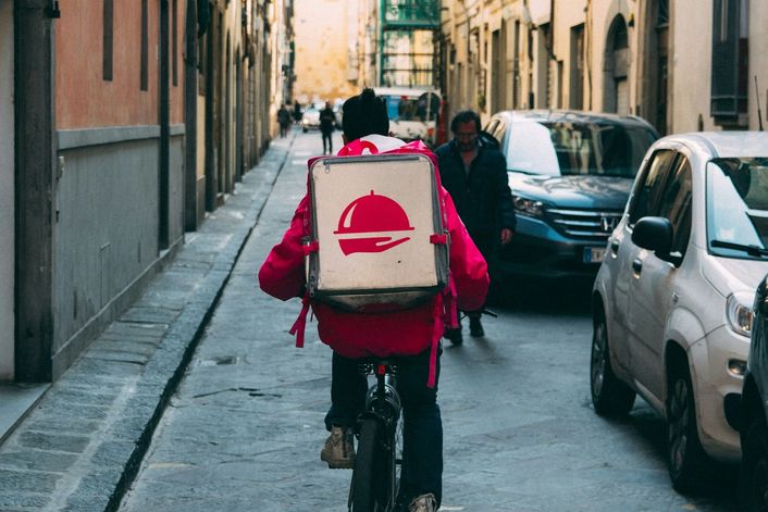 Een bezorger op de fiets met een bezorgbox op de rug in een smalle straat.