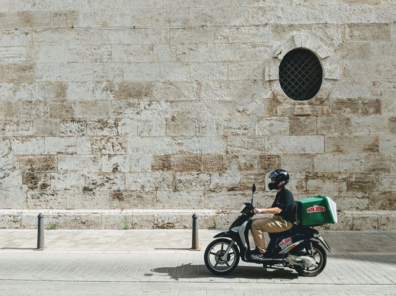 Een bezorgscooter met een bezorgbox rijdt langs een hoge natuurstenen muur.