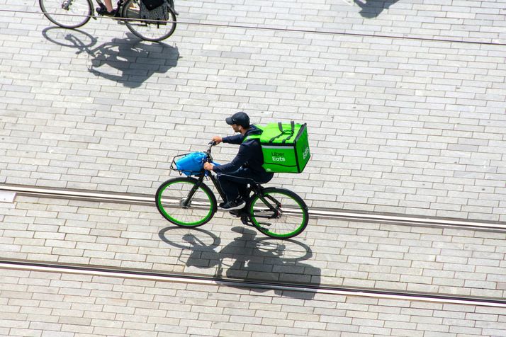 Van boven gezien fietst een bezorger met een groene bezorgbox over de klinkers.