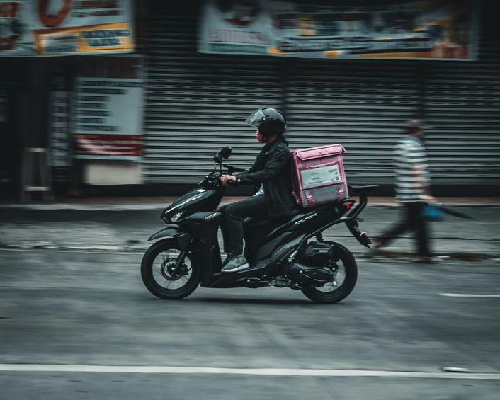 Een bezorger op een scooter met een roze bezorgbox rijdt door de straat.