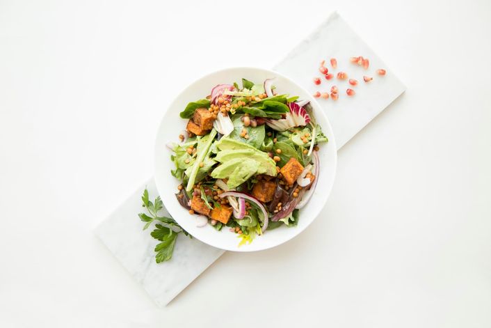 Een kom salade met pompoen en rode ui, van bovenaf op een marmeren plank.