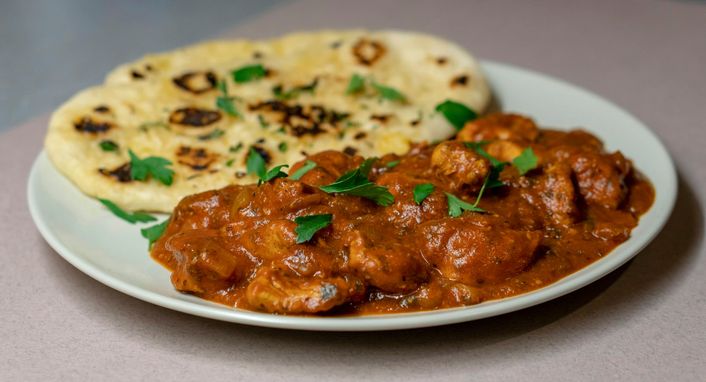 A plate of curry and naan bread, scattered with fresh coriander.