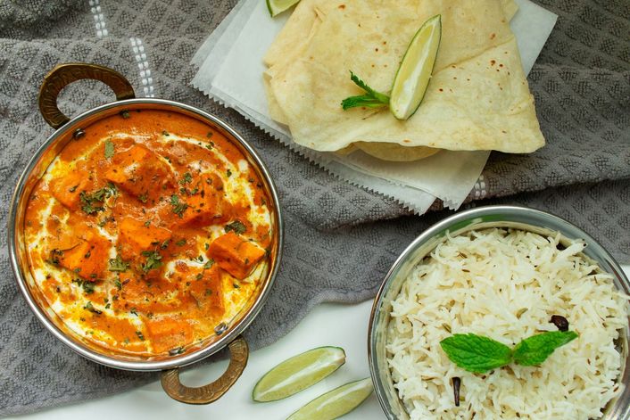 Een curry in een pan, met rijst en papadums ernaast.