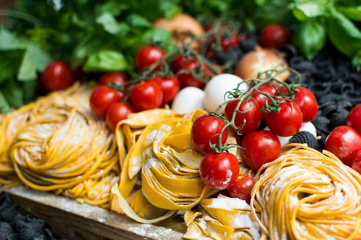 Nesten verse tagliatelle op een plank, met trostomaten, eieren en kruiden ernaast.