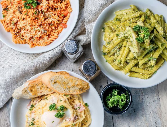Drie borden pasta van bovenaf, met knoflookbrood ernaast.