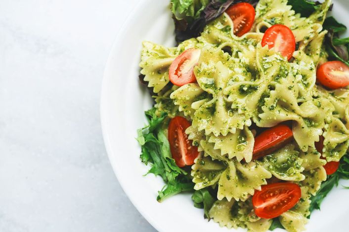 Farfalle with pesto, cherry tomatoes and rocket on a white plate.