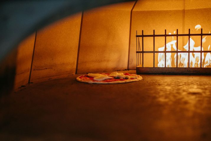 Een pizza bakt in een houtoven, met de vlammen achter in de oven.