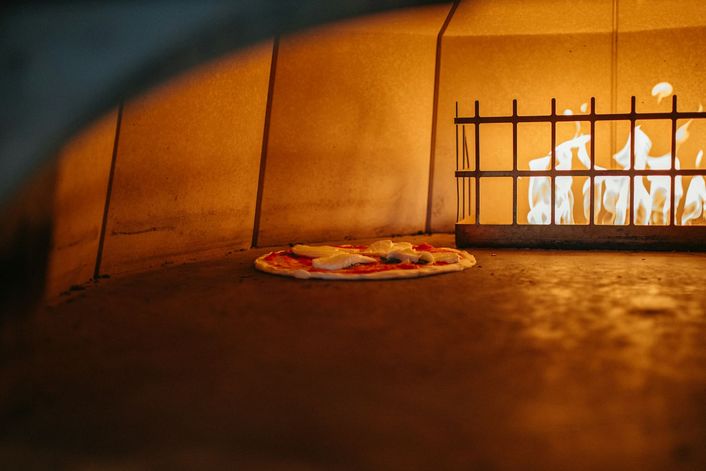 Een pizza in een houtoven, naast het vuur.