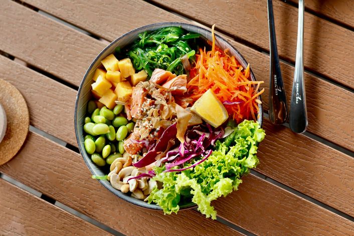 Een pokébowl met zalm, edamame en wortel, van bovenaf op een houten tafel.