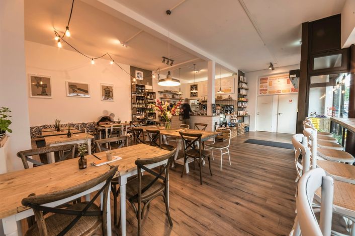 Een licht restaurant met houten tafels en een bar met bloemen achterin.