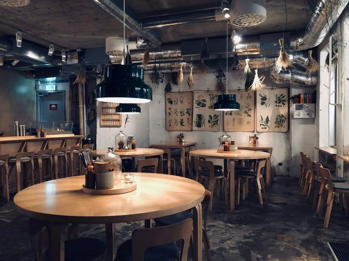 Ronde houten tafels onder lage lampen, met botanische prenten aan de muur.
