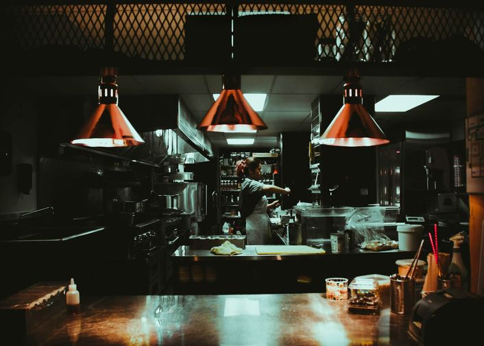 Three copper heat lamps hang above the pass of an otherwise dark kitchen.