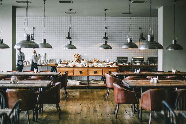Een ruime eetzaal met leren stoelen en een buffet onder stalen hanglampen.