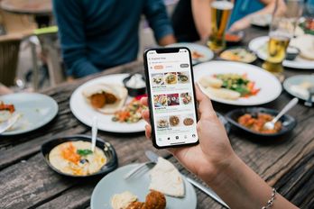 Een hand houdt een telefoon met een bestelapp boven een tafel vol schalen.