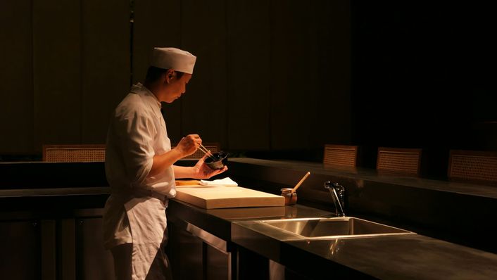 Een sushikok bereidt eten aan een verlichte toonbank in een donkere zaak.